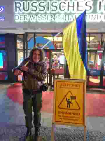 Henry Lindemeier vor dem Russischen Haus in Berlin neben einer ukrainischen Flagge und einem zweisprachigen Warnaufsteller.