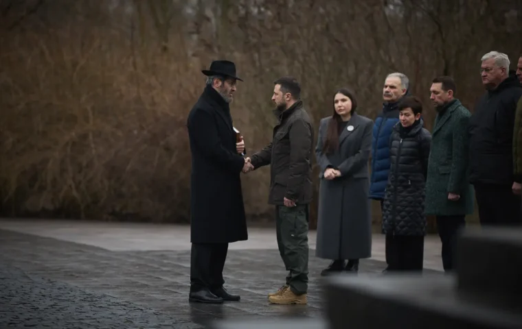 Präsident Wolodymyr Selenskyj begrüßt bei einer Gedenkzeremonie in Babyn Jar einen Rabbiner; weitere Teilnehmende stehen im Hintergrund.