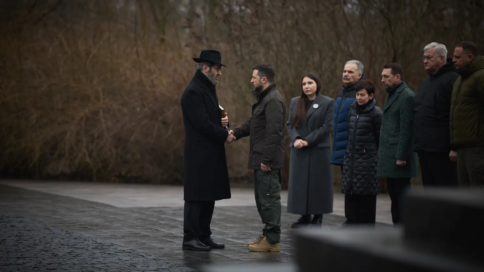 Präsident Wolodymyr Selenskyj begrüßt bei einer Gedenkzeremonie in Babyn Jar einen Rabbiner; weitere Teilnehmende stehen im Hintergrund.