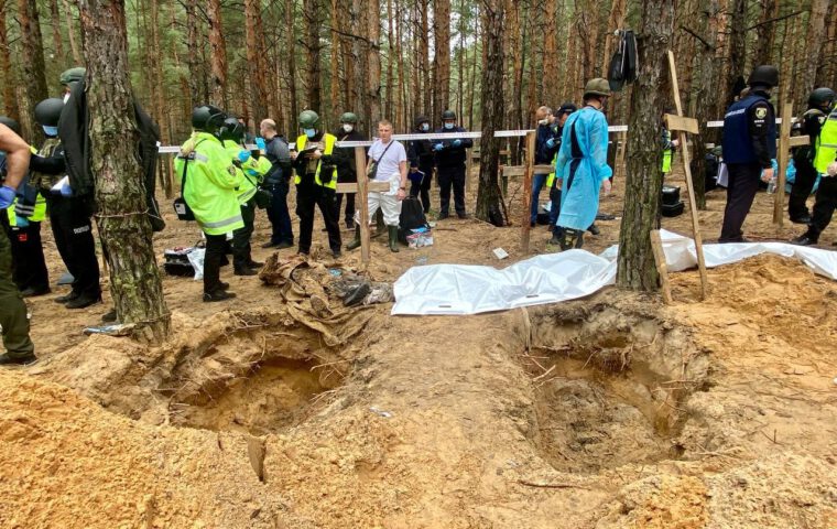 Ukrainische Ermittler und Forensiker arbeiten zwischen geöffneten Gräbern und Holzkreuzen auf dem Gräberfeld im Wald bei Izium.