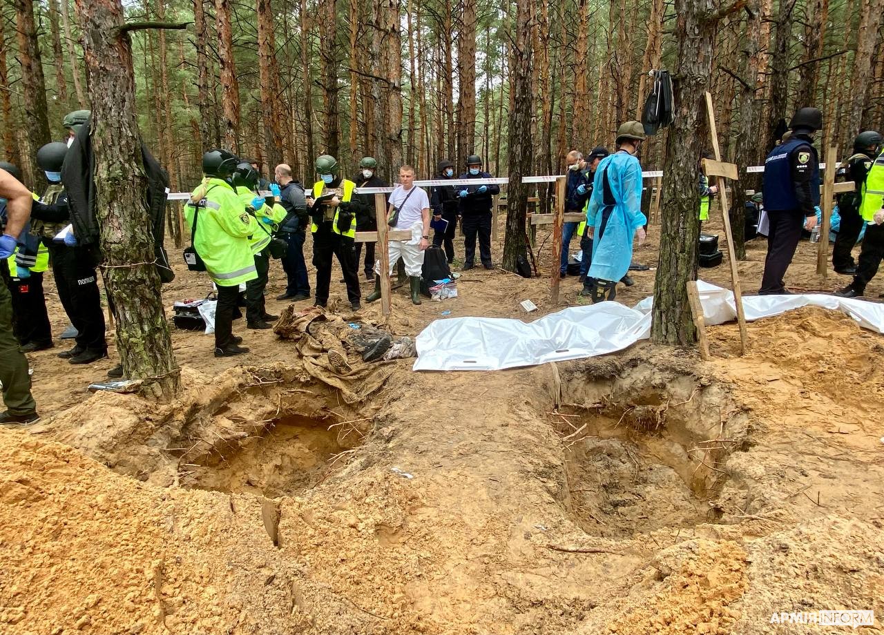 Ukrainische Ermittler und Forensiker arbeiten zwischen geöffneten Gräbern und Holzkreuzen auf dem Gräberfeld im Wald bei Izium.