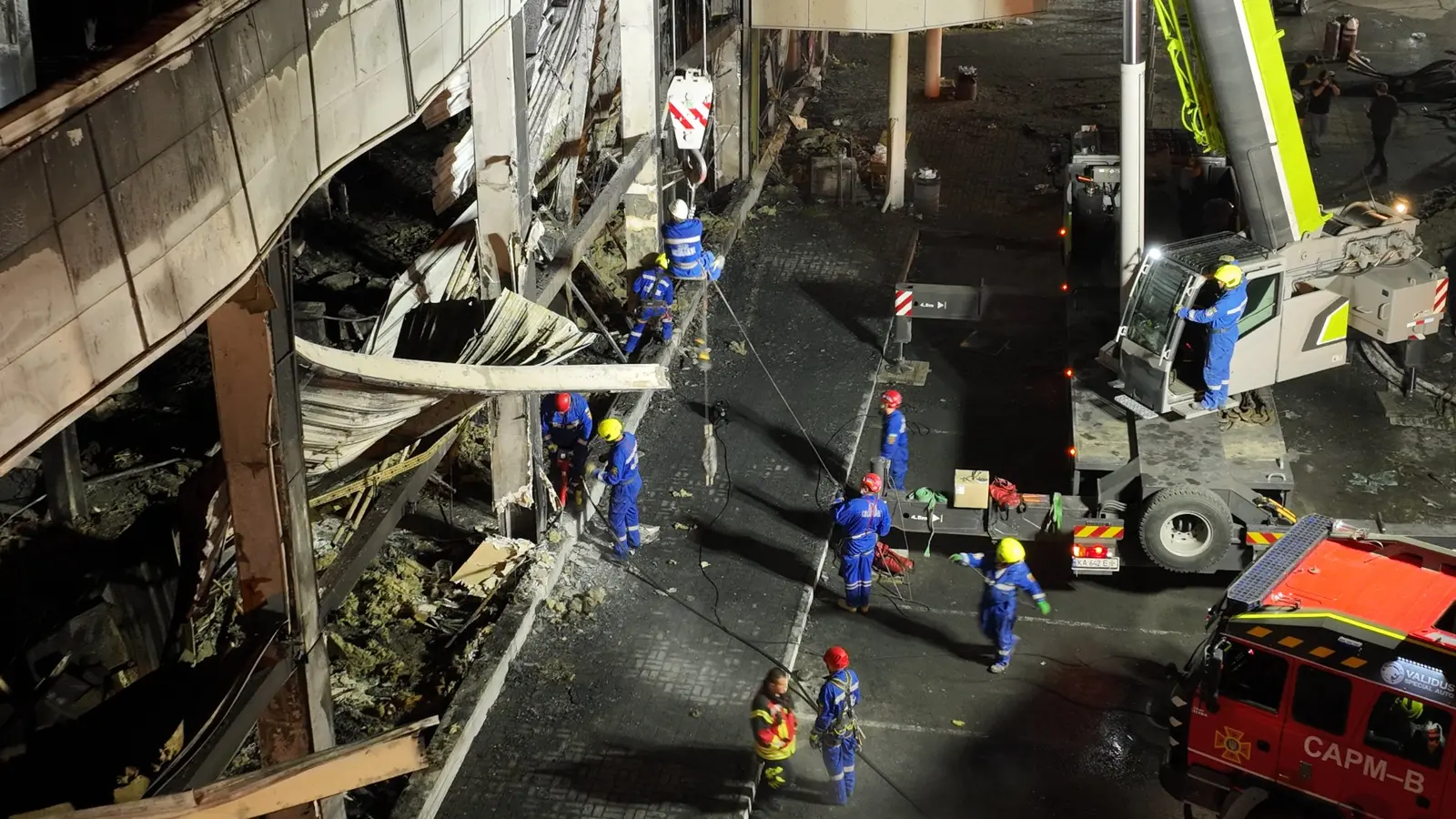 Ukrainische Rettungskräfte arbeiten nachts mit einem Kran an der zerstörten Außenwand des Einkaufszentrums Amstor in Krementschuk