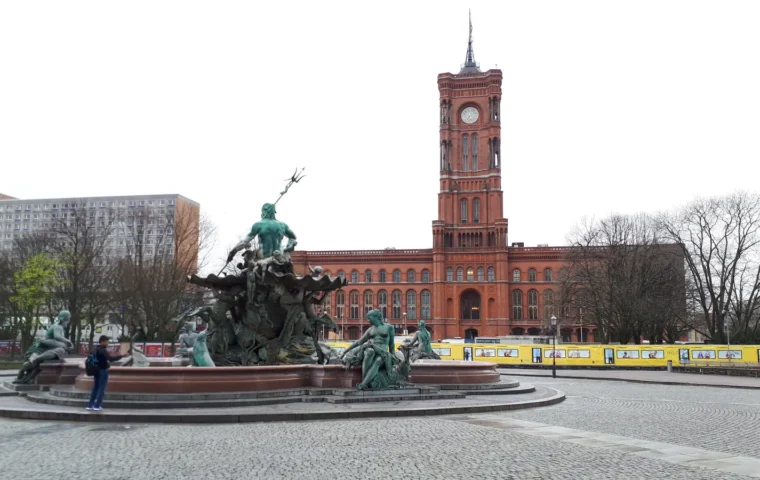 Das Rote Rathaus in Berlin hinter dem Neptunbrunnen unter einem bewölkten Himmel