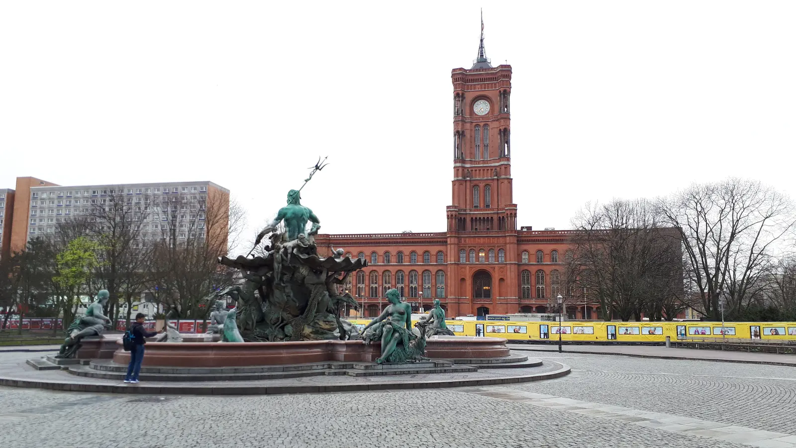 Das Rote Rathaus in Berlin hinter dem Neptunbrunnen unter einem bewölkten Himmel