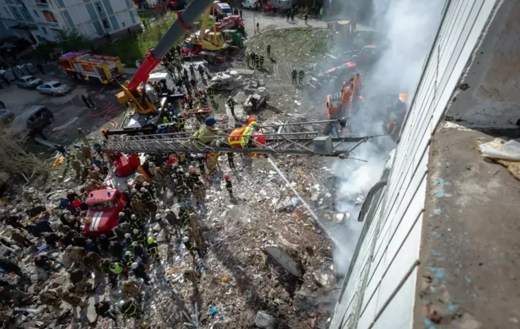 Blick von oben auf die Rettungsarbeiten am zerstörten Wohnhaus in Uman: Feuerwehrleute, Rettungskräfte, Kräne und Bagger arbeiten zwischen Trümmern und Rauch.