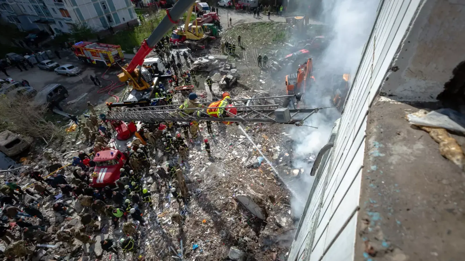 Blick von oben auf die Rettungsarbeiten am zerstörten Wohnhaus in Uman: Feuerwehrleute, Rettungskräfte, Kräne und Bagger arbeiten zwischen Trümmern und Rauch.